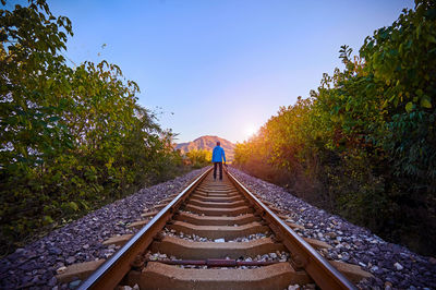 Rear view of man standing on railroad track against sky