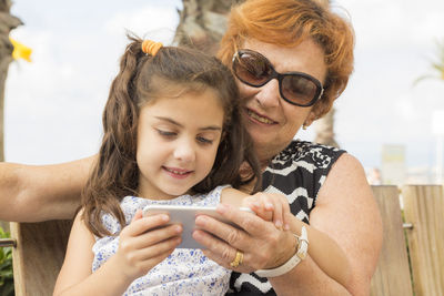 Grandmother with granddaughter using phone on bench