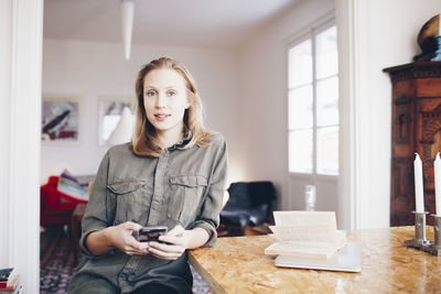 Portrait of young woman using mobile phone sitting by table at home