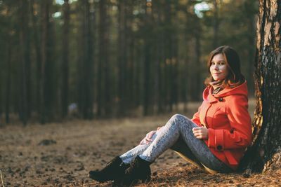 Portrait of young woman sitting against tree in forest