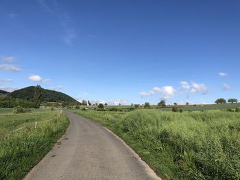 Empty road amidst field against sky