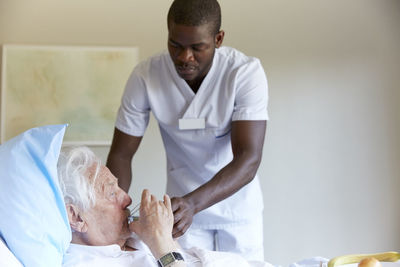 Male nurse feeding water to senior man in hospital ward