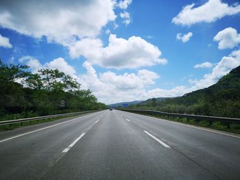 Empty road along trees and against sky