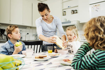 Mother serving breakfast to children at dining table in kitchen