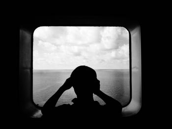 Silhouette of woman looking at sea through window