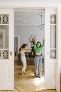 Full length of young female friends dancing in living room seen through doorway