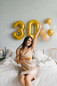Young smiling woman with long hair lies in bed with a cake on a plate and a candle and celebrates