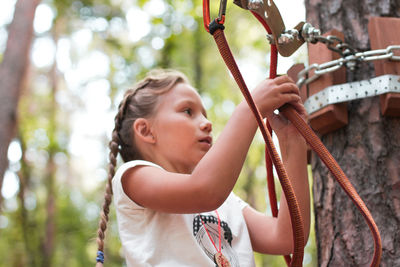 Low angle view of girl attaching safety harness on rope in forest