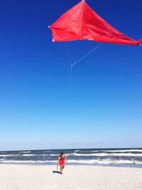 Man flying kite at beach against clear blue sky