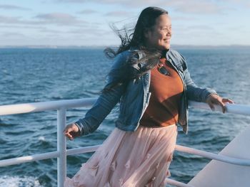 Smiling woman standing by railing against sea