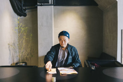 Man with papers sitting at table against wall