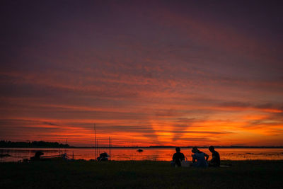 Silhouette people on beach against orange sky