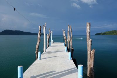 View of wooden posts in calm sea against blue sky