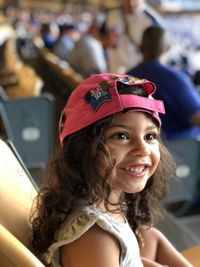 Close-up of smiling girl wearing cap sitting at stadium
