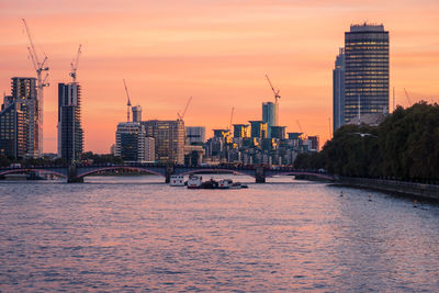 Bridge over river by buildings against sky during sunset