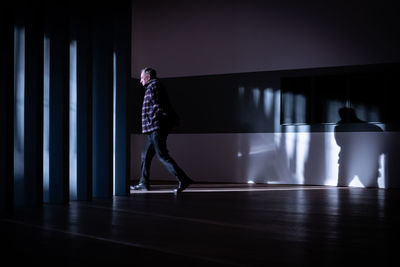 Side view of man standing against illuminated wall