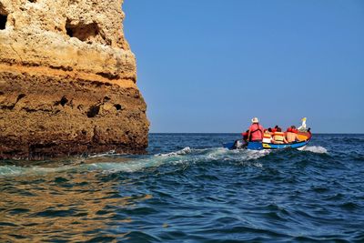 People on boat in sea against clear sky during sunny day