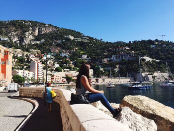 Woman sitting by buildings against clear sky