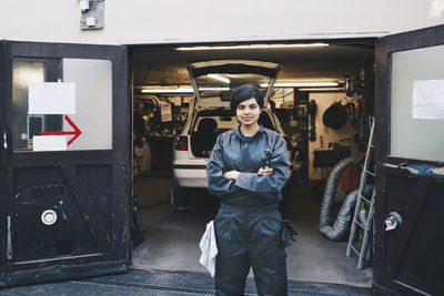 Portrait of confident female mechanic standing at entrance of auto repair shop