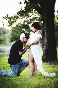 Full length of young woman standing on field while father-to-be loves his daughter in womb