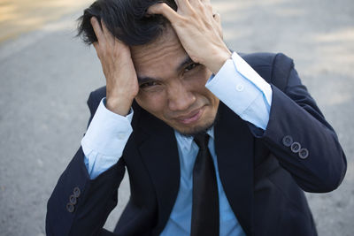 High angle portrait of stressed businessman with head in hands sitting on road