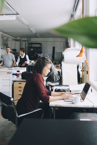 Side view of businesswoman using laptop at desk in creative office