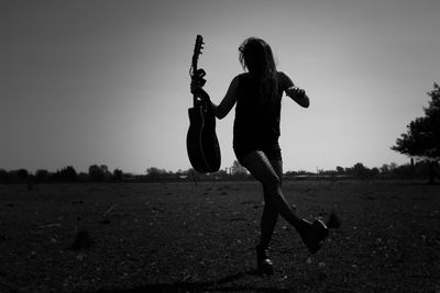 Silhouette woman holding guitar while standing on field against clear sky