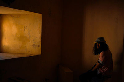 Side view of woman sitting against wall at home