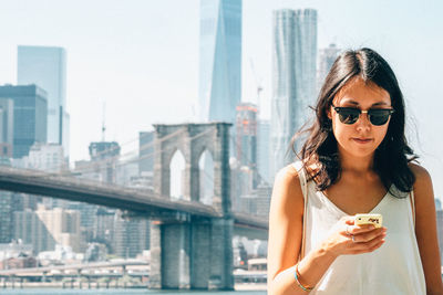 Young woman using smart phone against brooklyn bridge