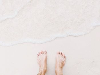 Low section of person standing on wet sand