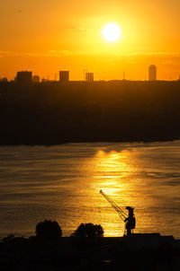 Silhouette man fishing in sea against orange sky