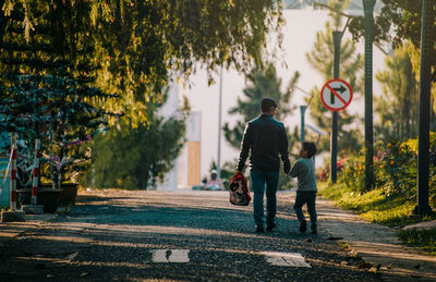 Full length rear view of father walking on road