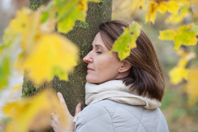 Portrait of young woman looking at plant during winter