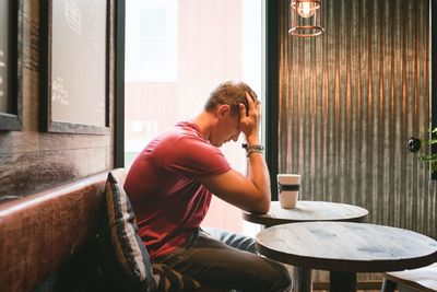 Man sat feeling stressed with his face in his hands in a cafe
