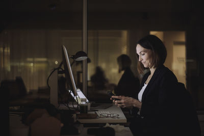 Businesswoman using smart phone while working overtime at work place