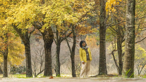 Rear view of woman standing amidst trees in forest during autumn
