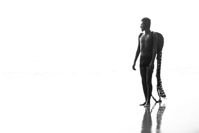 Full length of shirtless model with costume wing at beach against clear sky