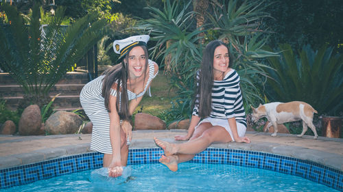 Portrait of smiling friends at poolside against plants in park