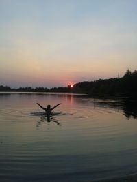 Silhouette shirtless man enjoying in lake against sky during sunset