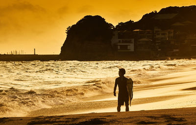 Rear view of silhouette man standing at beach during sunset