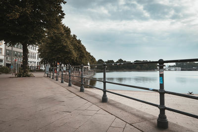 Footpath by river in city against sky