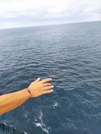 Person hand by sea against sky