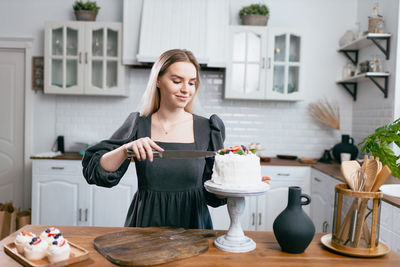 Smiling woman cutting cake at kitchen