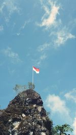 Low angle view of flag on rock against sky