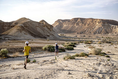 Rear view of 2 kids running between mountain against sky