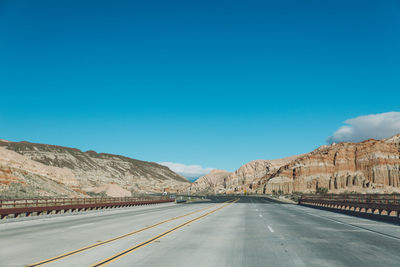 Empty road by mountains against clear blue sky