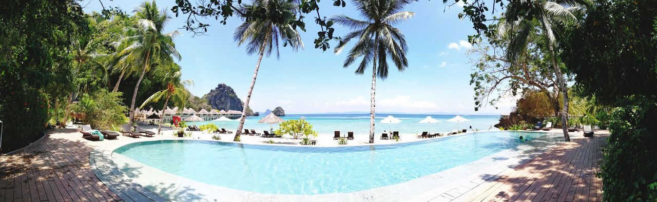 swimming pool, water, tree, palm tree, tourist resort, blue, beauty in nature, panoramic, nature, sunlight, sky, vacations, scenics, day, summer, outdoors, no people