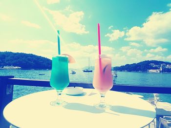 Close-up of drink on table by sea against sky