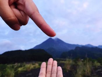 Close-up of hands gesturing over mountains against sky