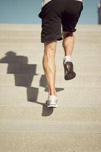 Back view of cropped unrecognizable athletic male running upstairs while training on sunny day in city in summer